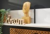Zbliżenie na dekoracje na półce Remo drewniany napis dream, rzeźba twarzy oraz wisząca roślina na tle ciemnej ściany